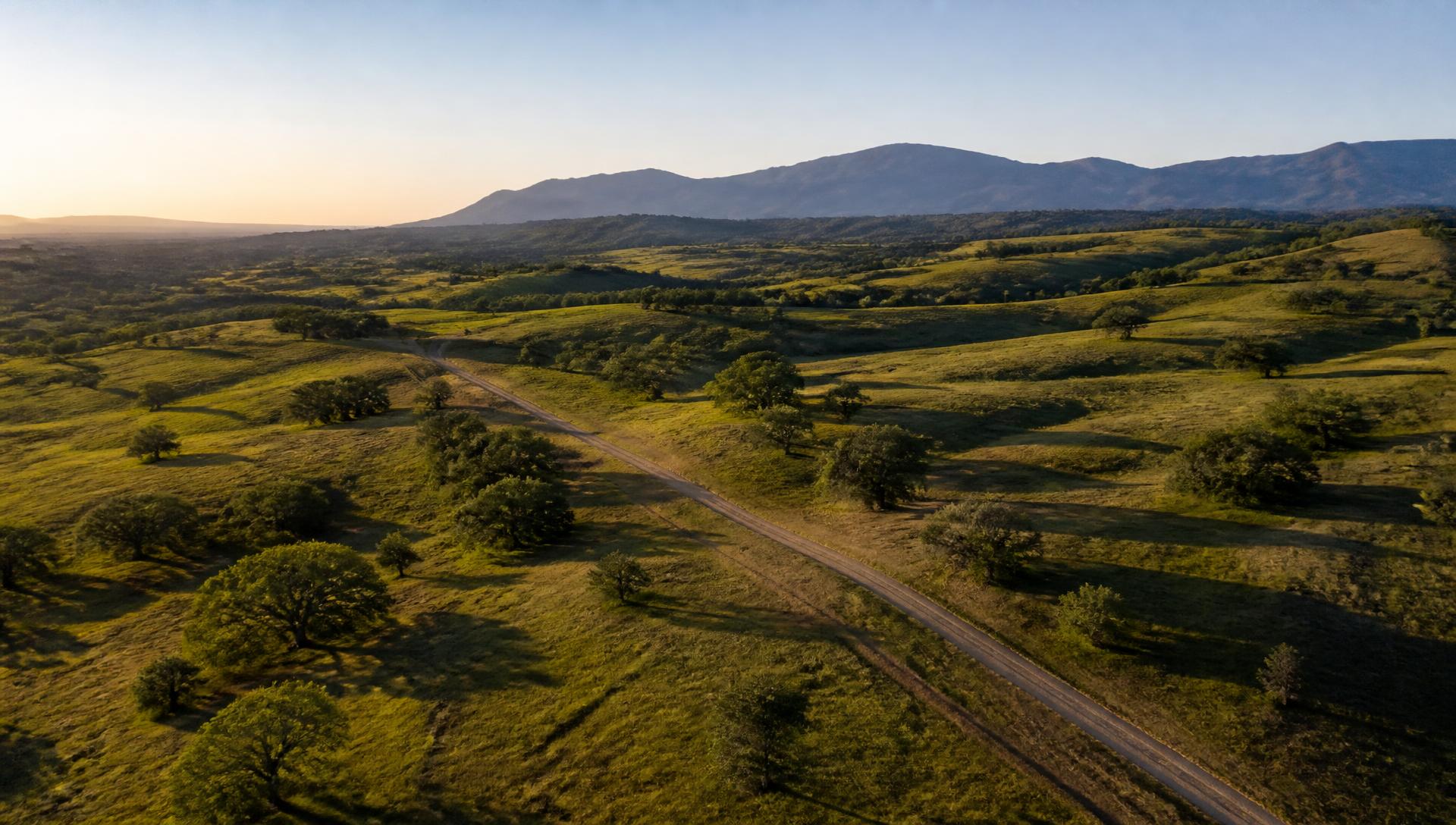 Aerial view of open rural acreage at sunset with a dirt access road